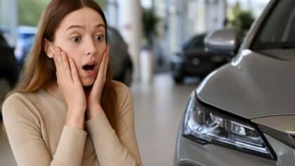 Jeune femme surprise des différents malus écologique dans une concession automobile moderne devant une voiture grise brillante