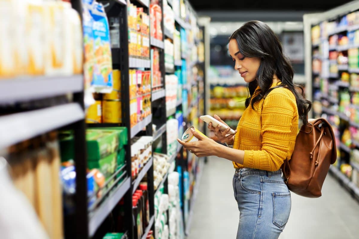 Une femme comparant les prix dans les rayons d'un supermarché.